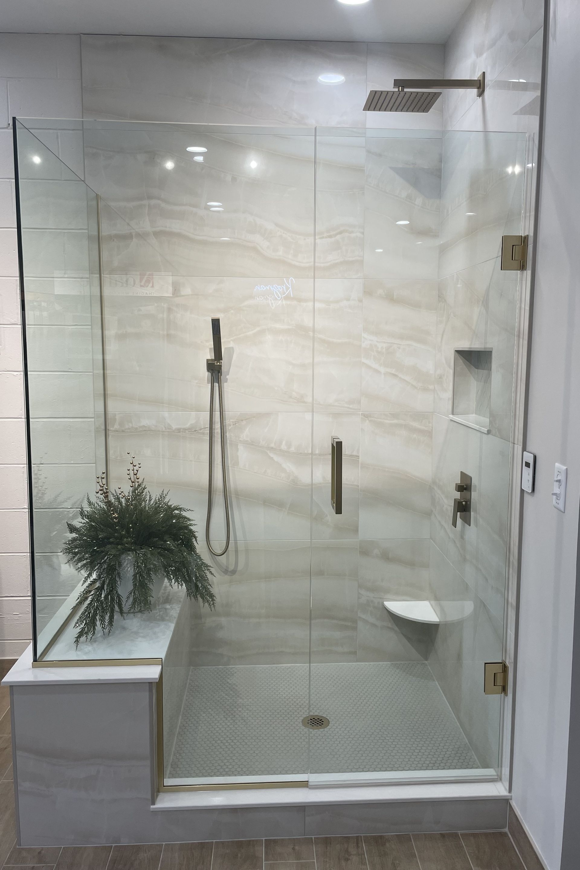 Glass-enclosed modern shower with white tile, marble bench, and a potted plant on the ledge