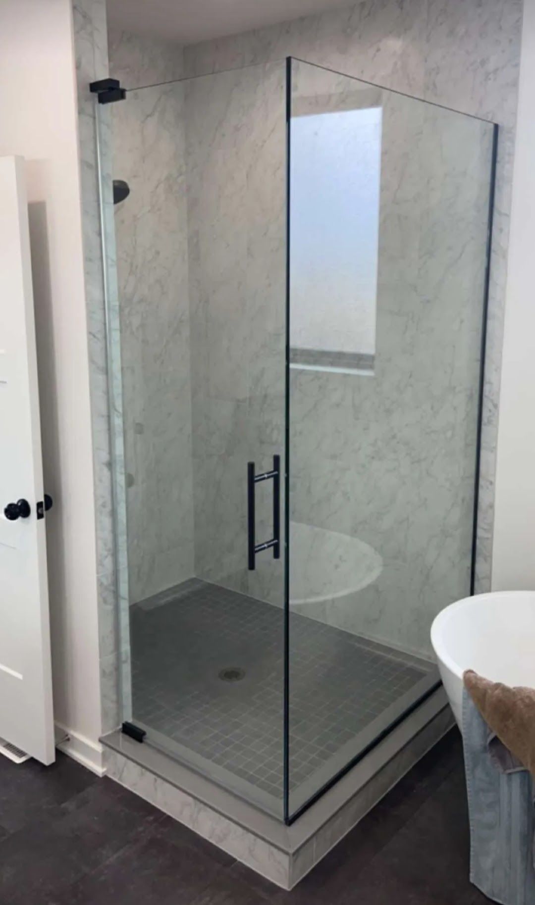 Glass shower enclosure with chrome handle and gray tiled bathroom floor