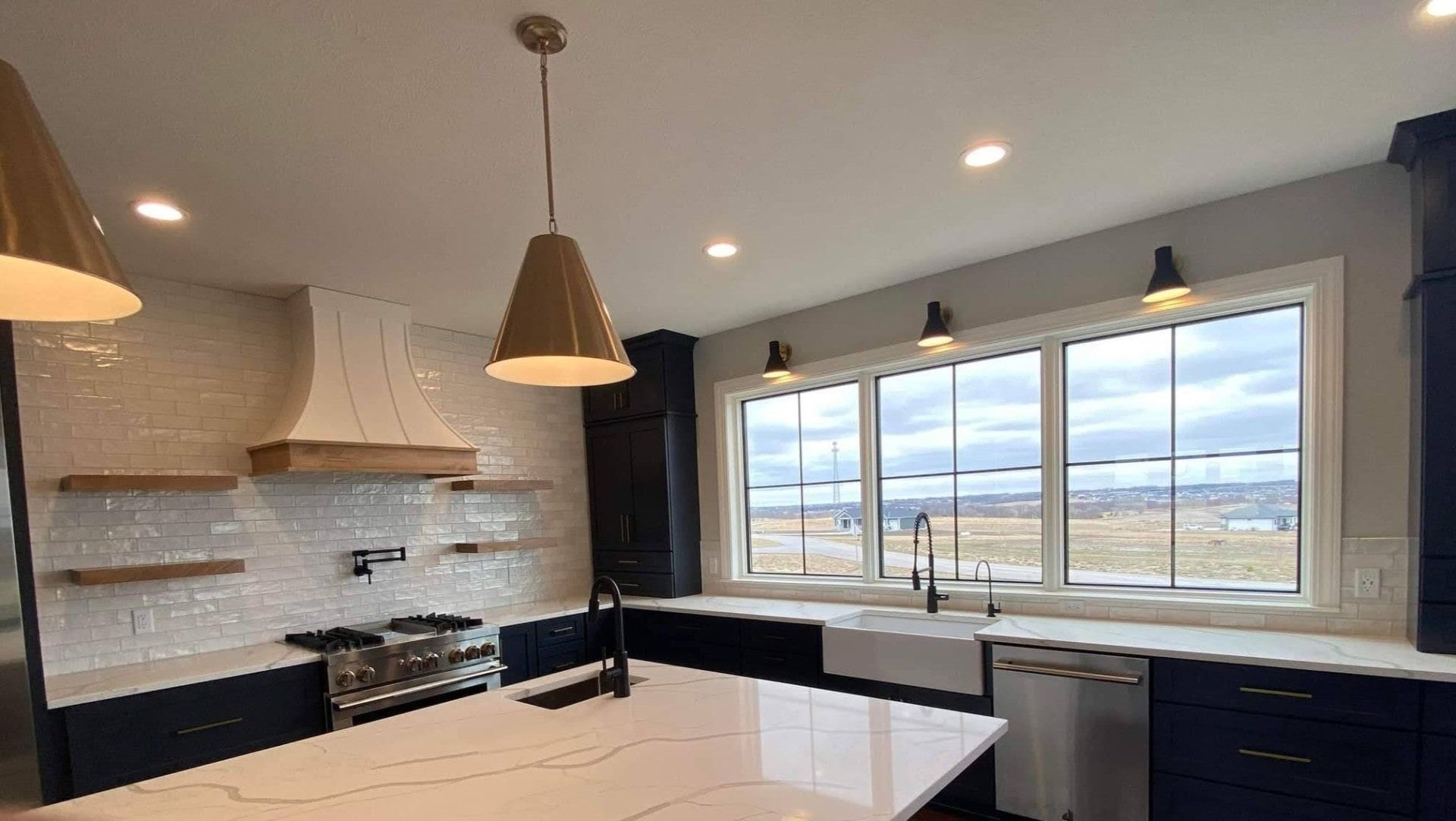 Modern kitchen with white island, dark cabinets, pendant lights, and large window overlooking a snowy landscape