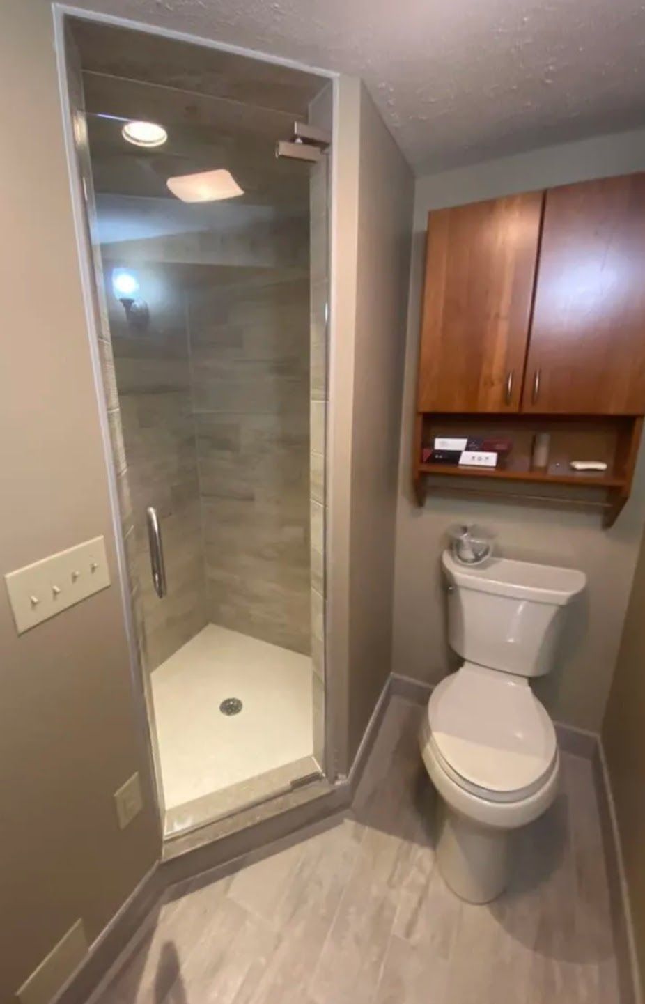 Compact bathroom with glass shower, toilet, and wood cabinet