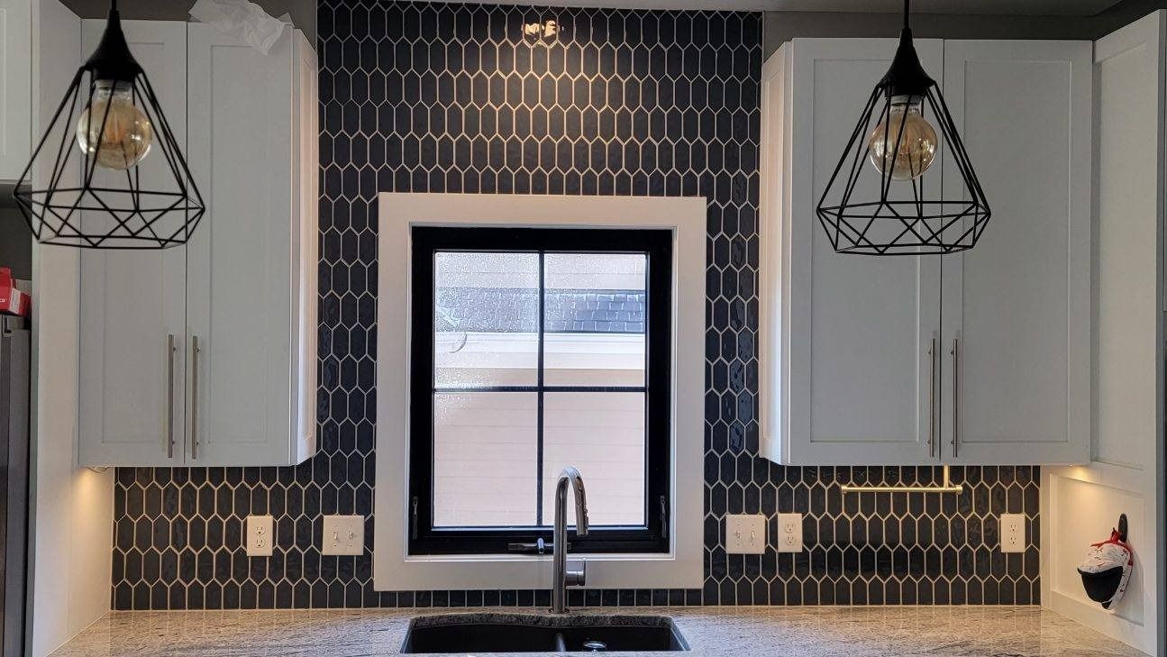 Modern kitchen sink with black-and-white tile backsplash, white cabinets, and pendant lights, viewed straight on