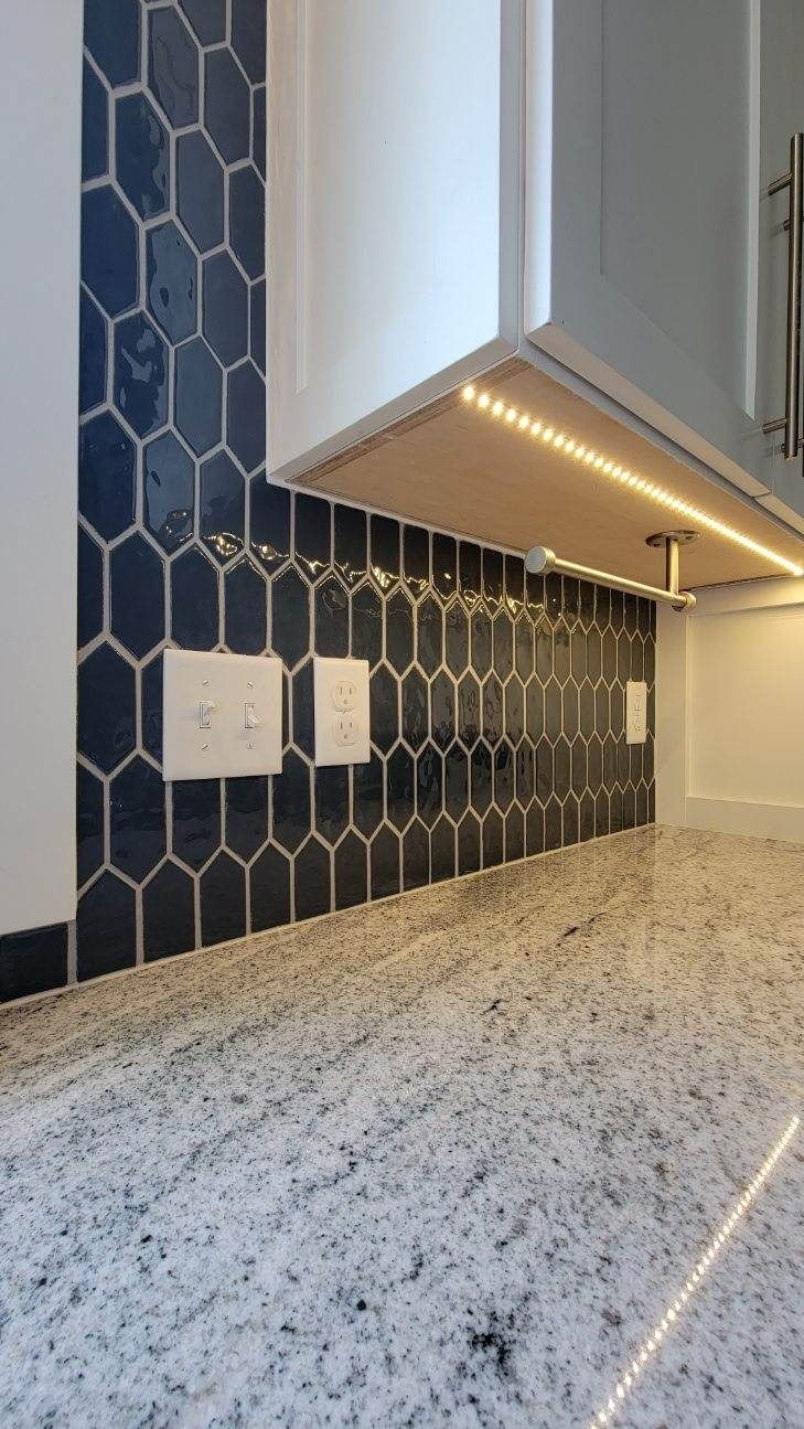 Modern kitchen counter with speckled granite, dark hex tile backsplash, white cabinets, and under-cabinet lighting