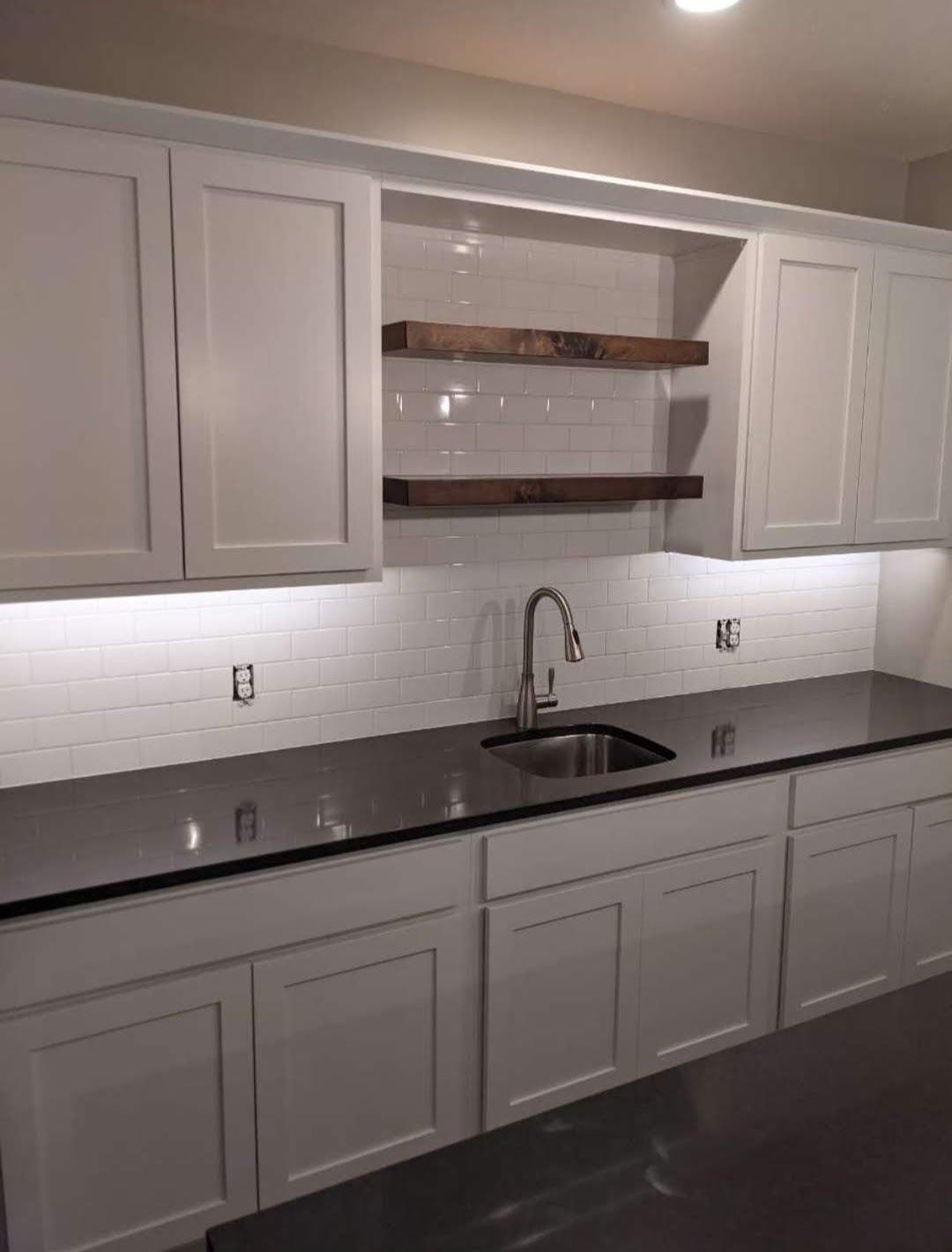Modern kitchen with white cabinets, black countertops, and a sink under open shelves
