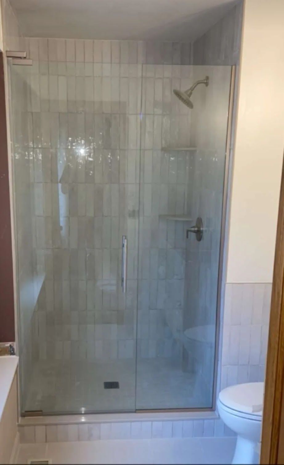 Glass shower enclosure in a tiled bathroom with a showerhead and toilet beside it.