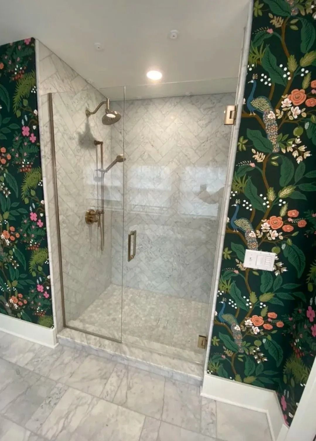 Glass walk-in shower with marble tile and tropical wallpaper accents
