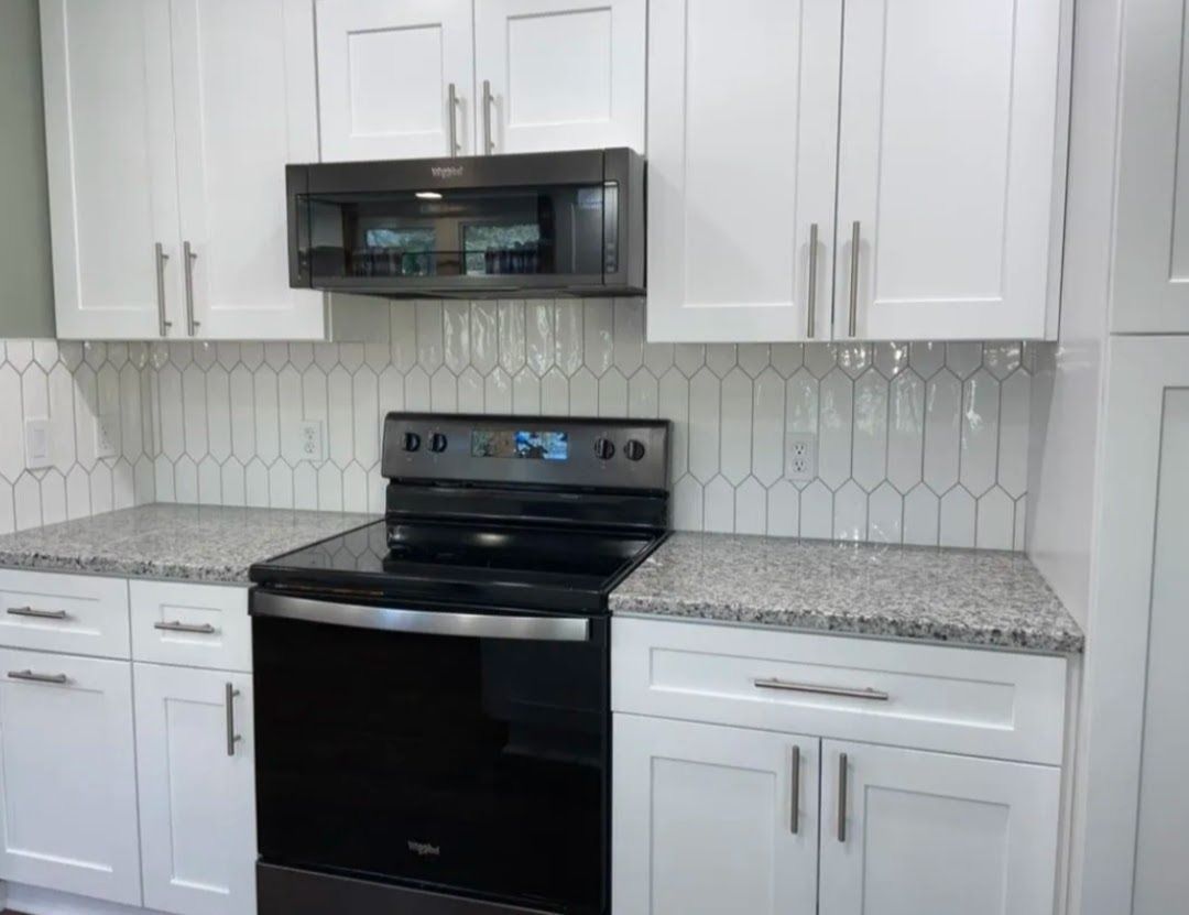 Modern kitchen with white cabinets, black appliances, gray countertops, and hexagon tile backsplash