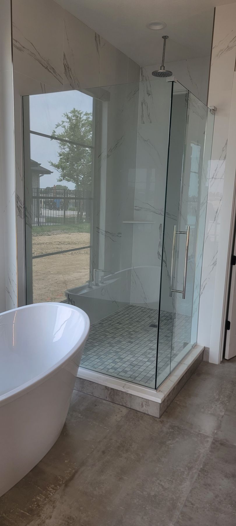 Modern bathroom with glass shower enclosure, white freestanding tub, and tiled floor