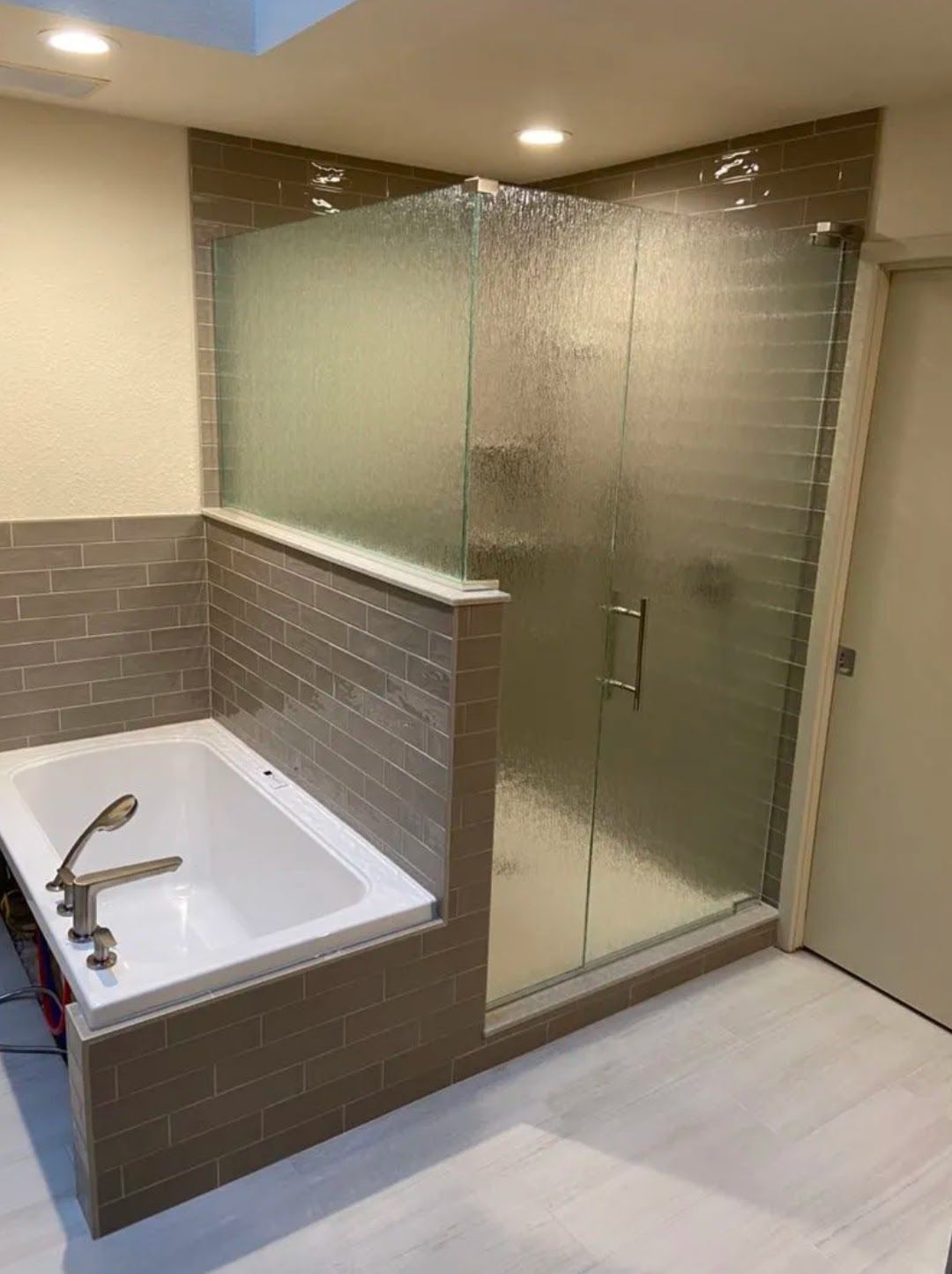 Accessible bathroom with a bathtub, frosted glass shower enclosure, and beige tile walls.