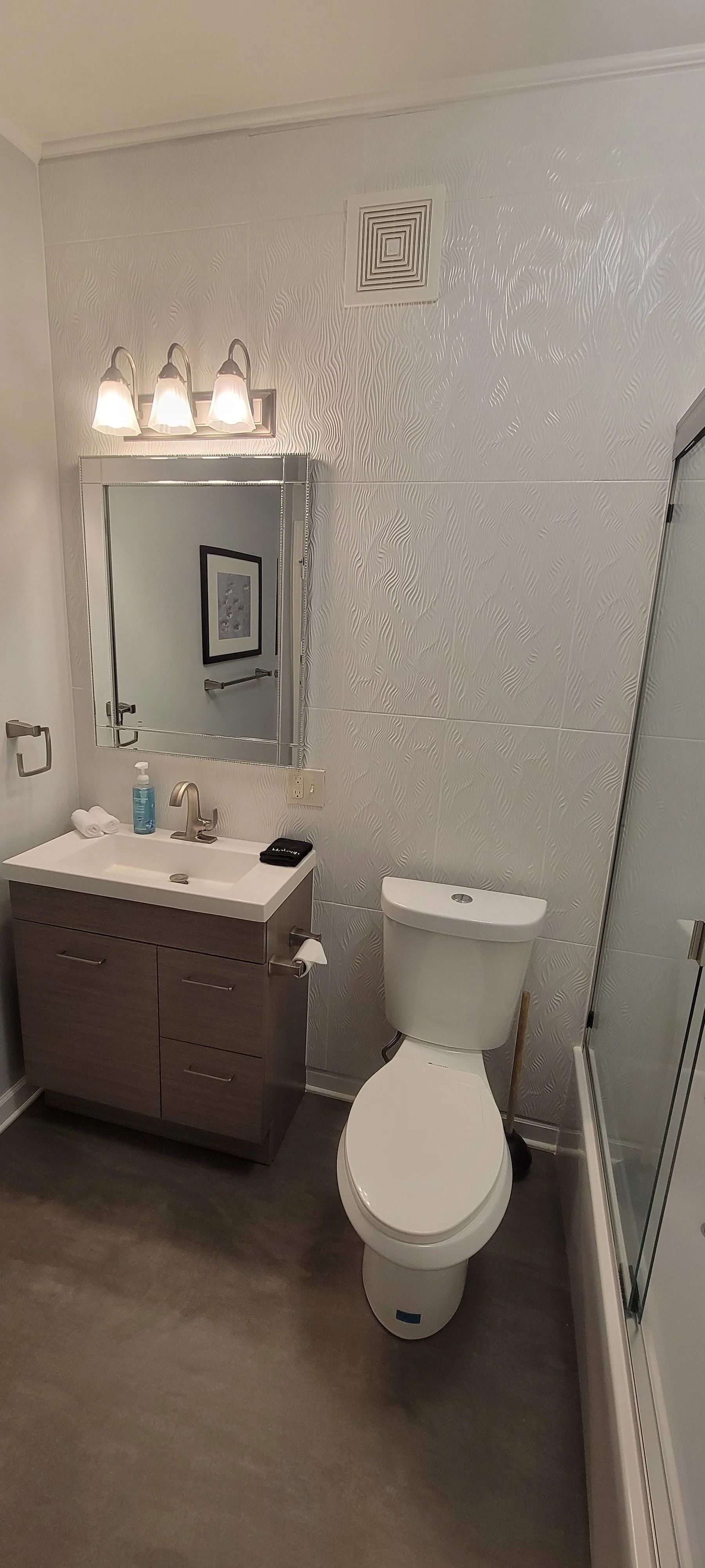 Small bathroom with pedestal sink, toilet, large mirror, and white tiled walls.