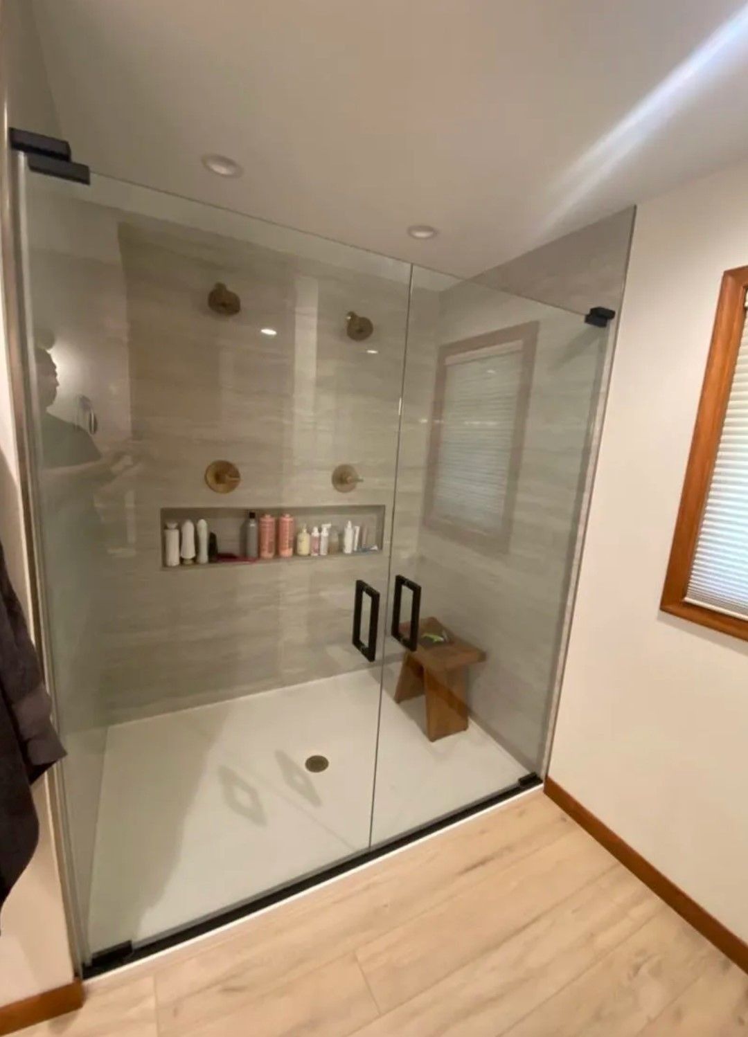 Modern glass-enclosed shower with beige tile, built-in shelf, and wooden bench in a bathroom