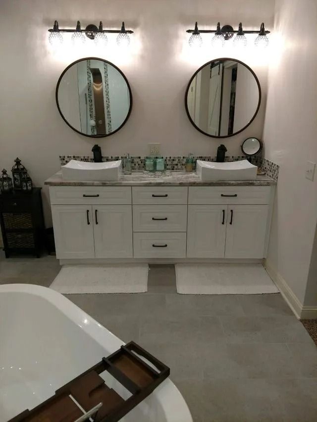 Modern bathroom with double vanity, round mirrors, wall sconces, and a bathtub in the foreground