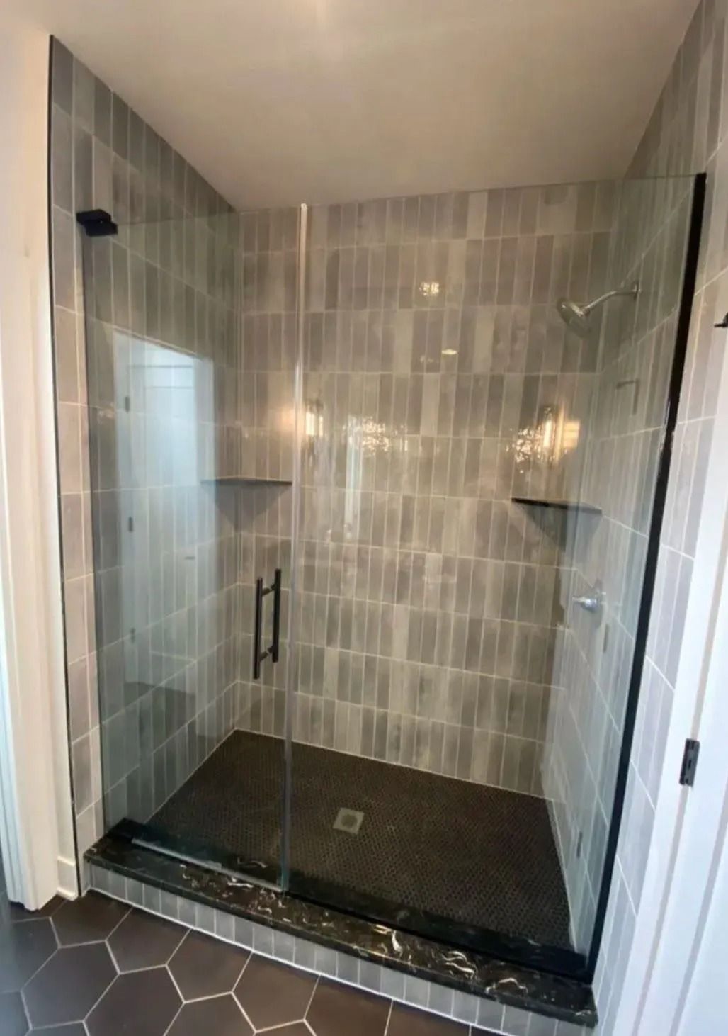 Walk-in tiled shower with glass enclosure and black shower pan, viewed from the doorway