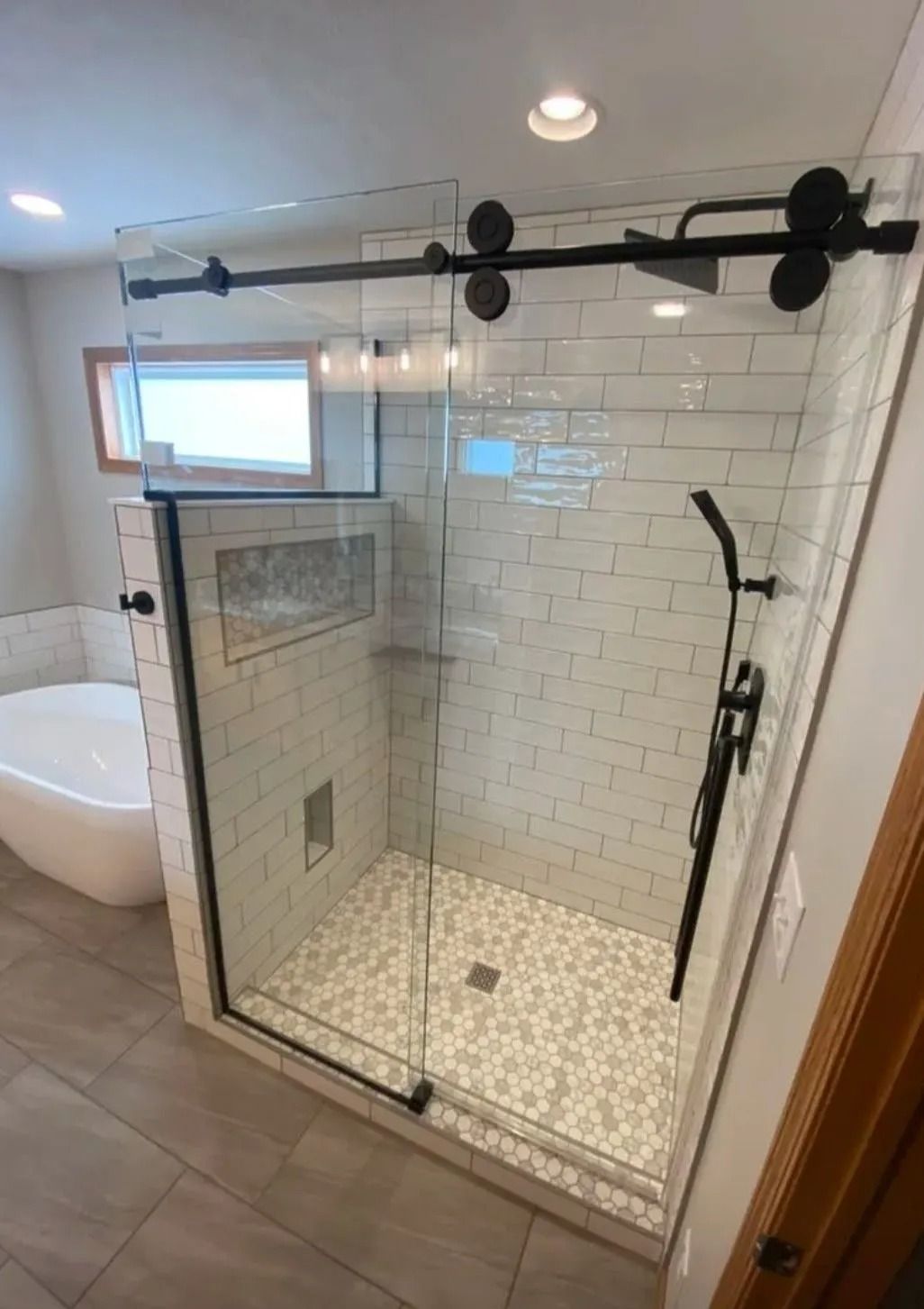Glass walk-in shower with black hardware, white tile walls, and pebble floor in a modern bathroom