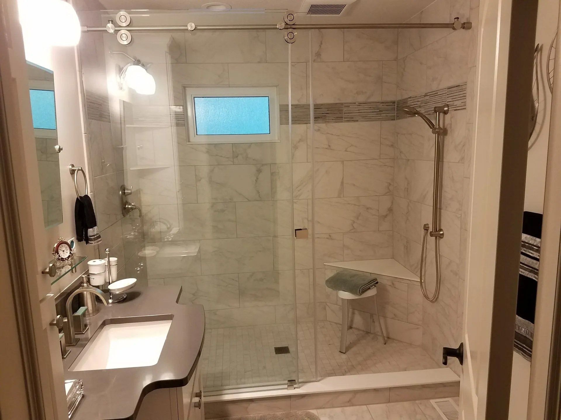 Accessible bathroom with walk-in shower, grab bars, bench, and sink beside tiled walls.