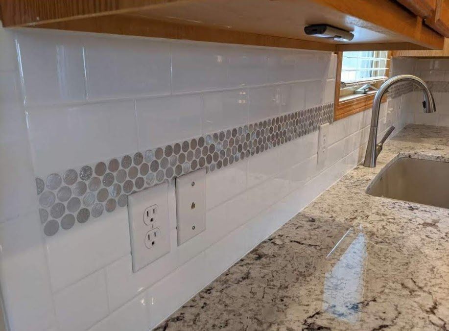 Kitchen backsplash with white subway tile, gray accent strip, outlet, and granite countertop beside a sink.