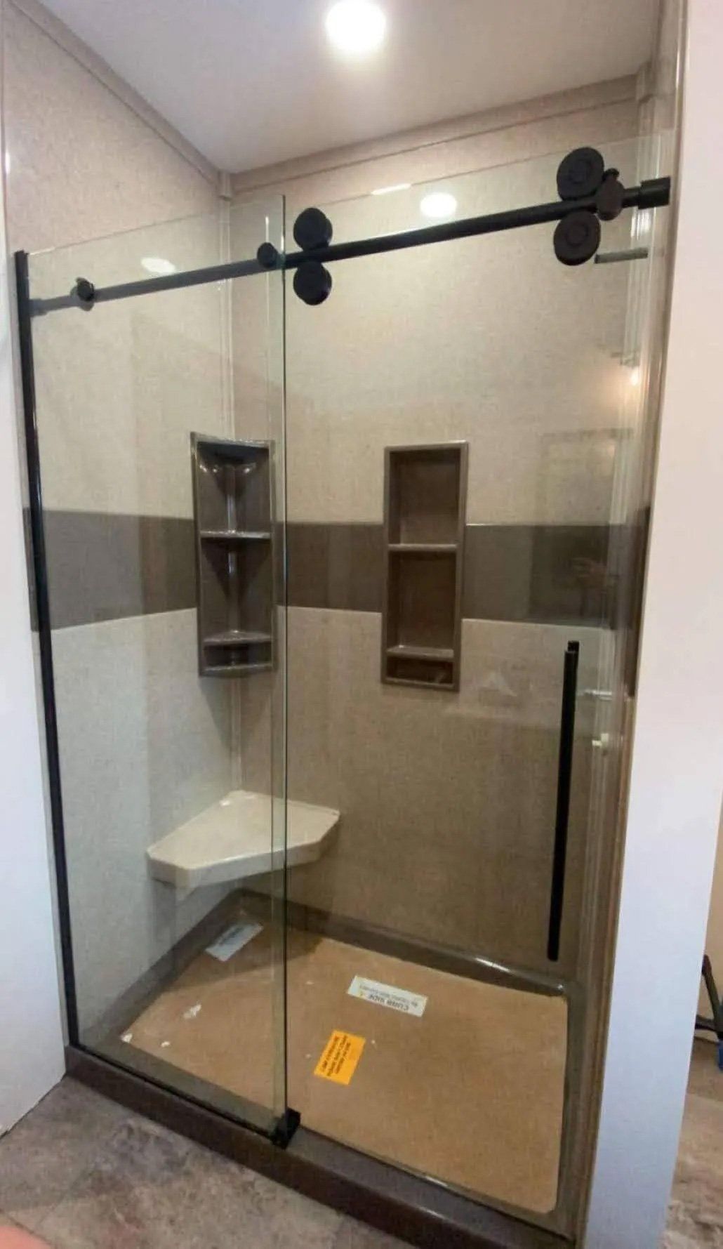 Glass shower stall with black frame, built-in shelves, and bench in a tiled bathroom