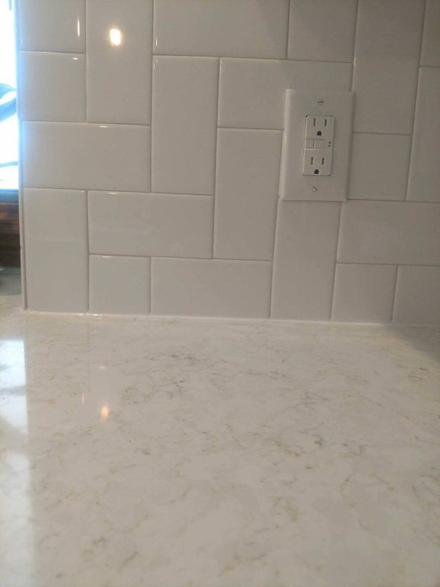 White tiled kitchen backsplash above a light marble countertop with a white electrical outlet.