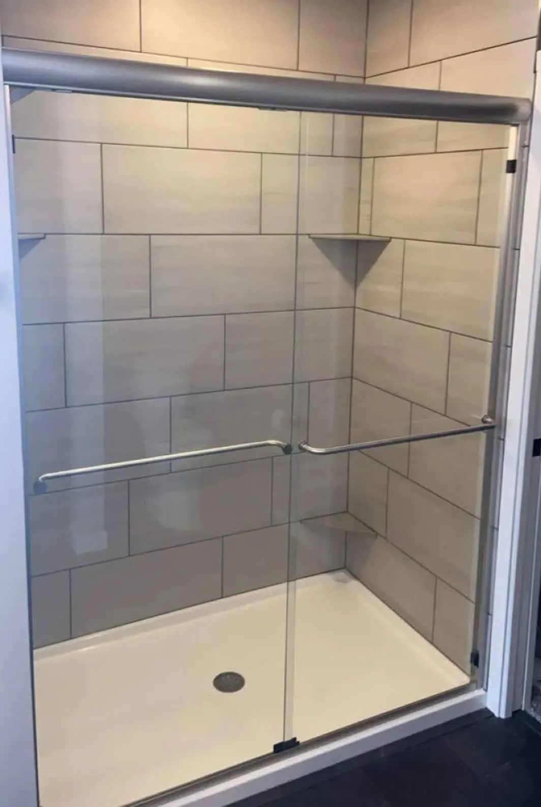 Modern tiled walk-in shower with glass doors and chrome grab bars