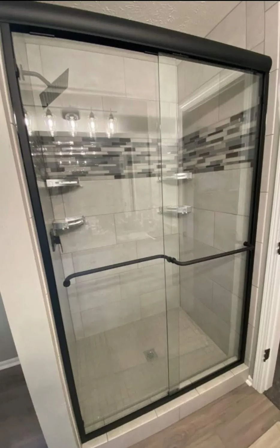 Glass shower enclosure with black frame and tiled bathroom walls