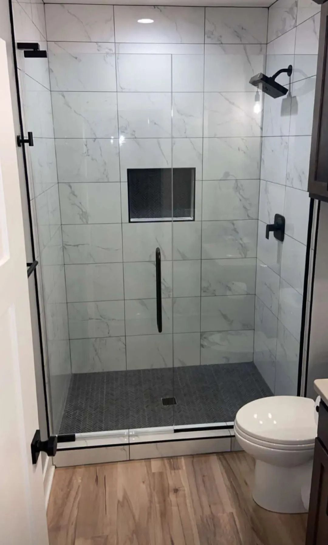 Modern bathroom with a glass shower enclosure, white tile walls, and wood-look floor.