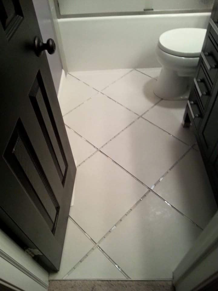 Small bathroom with white tiled floor, dark cabinets, and a white toilet.