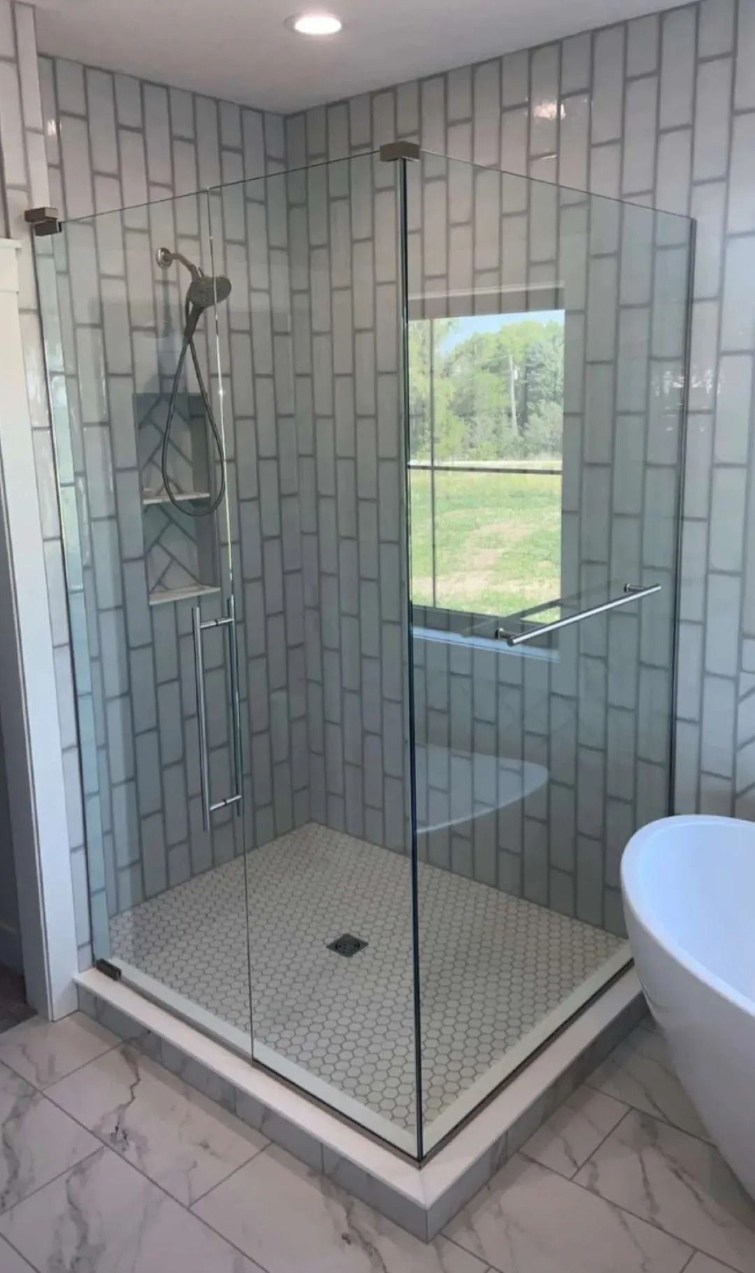Glass shower with white subway tile, mosaic floor, and window overlooking a green yard