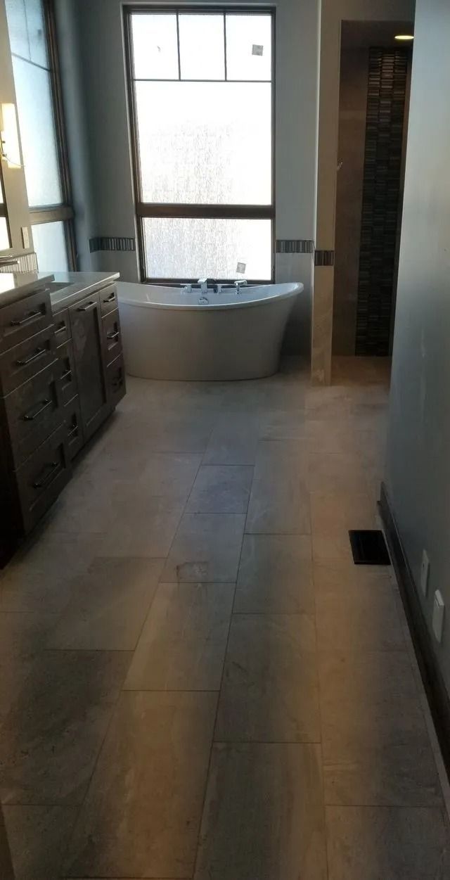 Modern bathroom with a freestanding tub, window, vanity, and tiled floor.