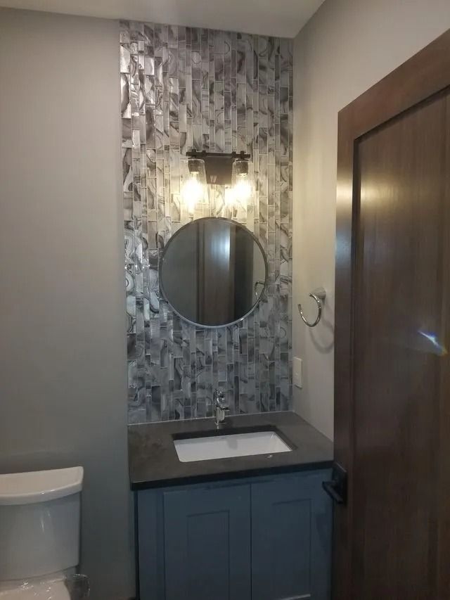 Small bathroom vanity with round mirror, wall sconce, blue cabinet, and wood door.