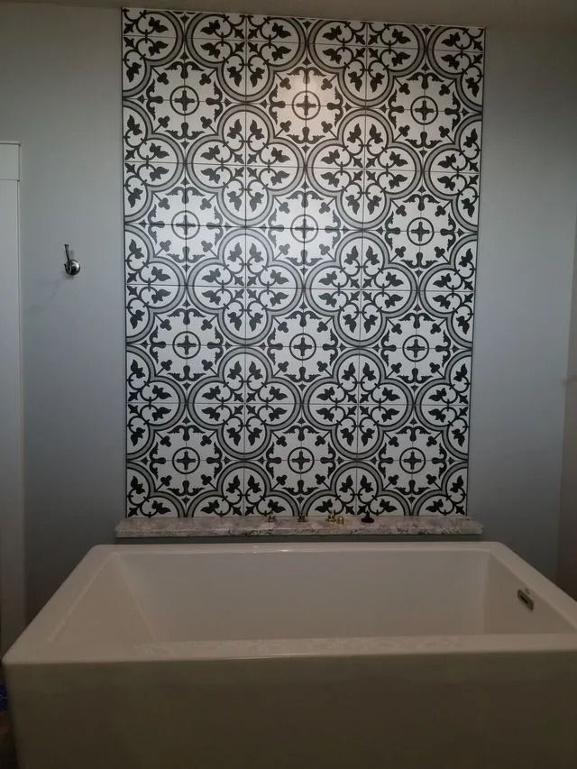Bathroom with a white bathtub and patterned black-and-white tile accent wall.