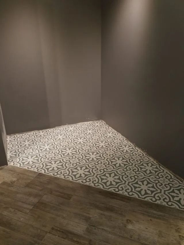 Small empty room corner with dark walls, patterned tile floor, and wood flooring edge