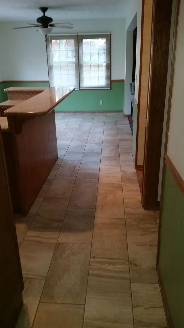 Empty hallway with tiled floor, green walls, and a window at the far end.