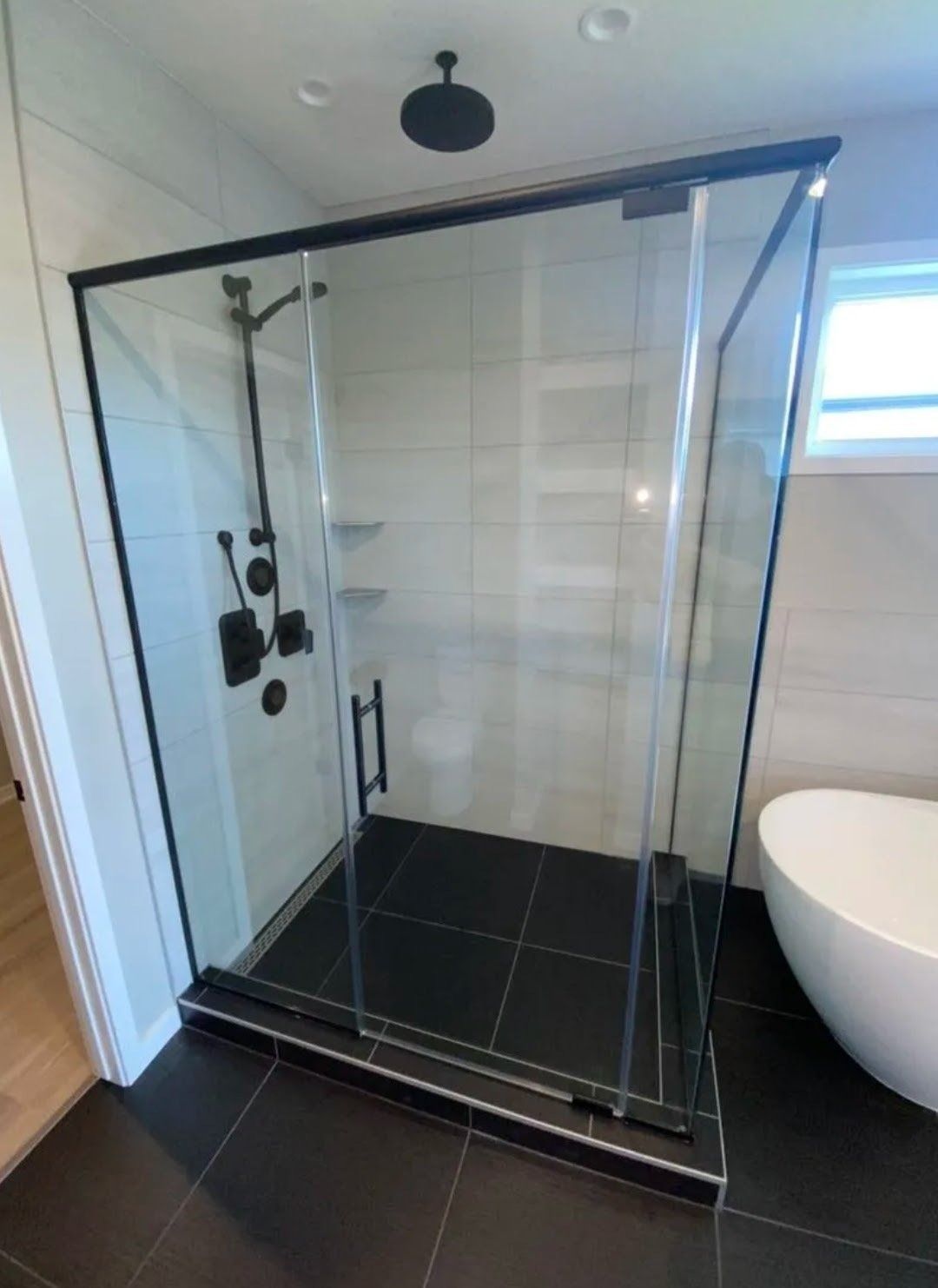 Modern bathroom with glass shower enclosure, black tile floor, and white tiled walls