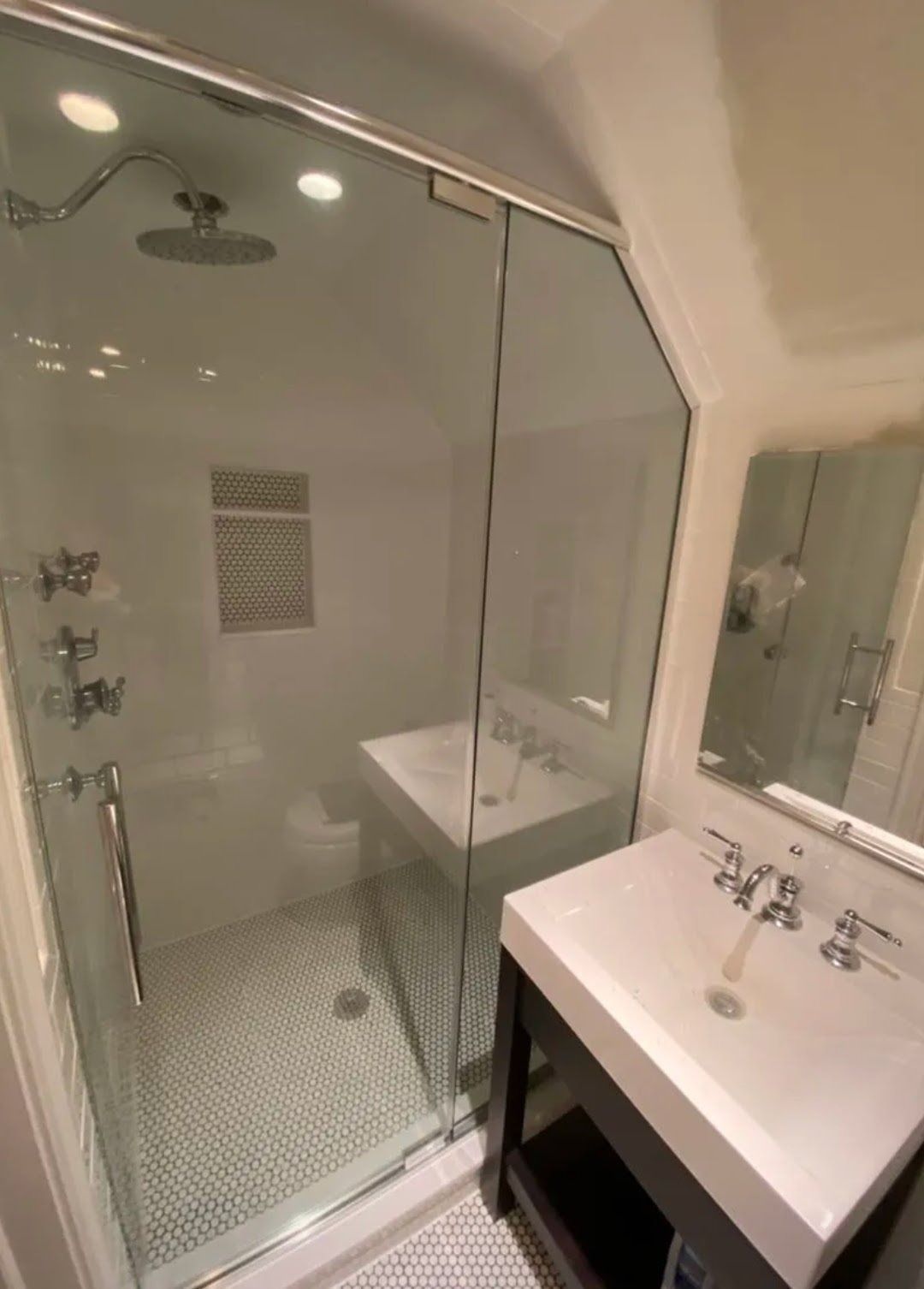 Glass shower beside white vanity in a modern bathroom with recessed lights and mosaic tile floor
