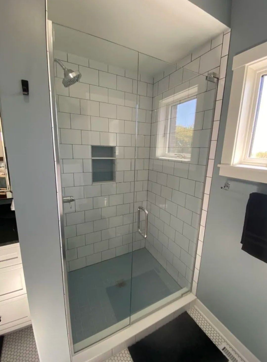 Walk-in shower with white subway tile, clear glass door, and small frosted window.