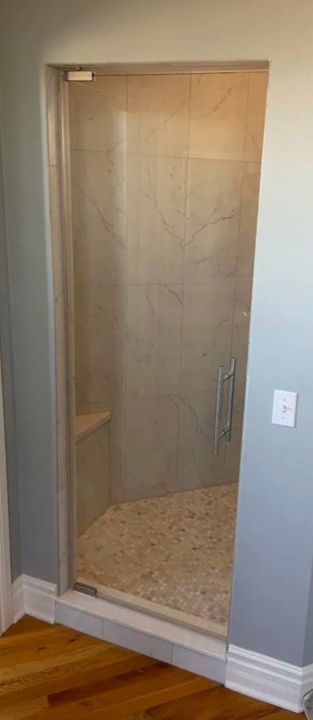 Glass shower stall beside a gray wall, with beige tile and hardwood floor visible