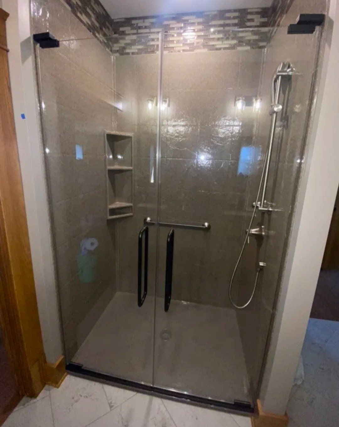 Glass shower enclosure with dark tile walls, wall shelves, and a handheld showerhead