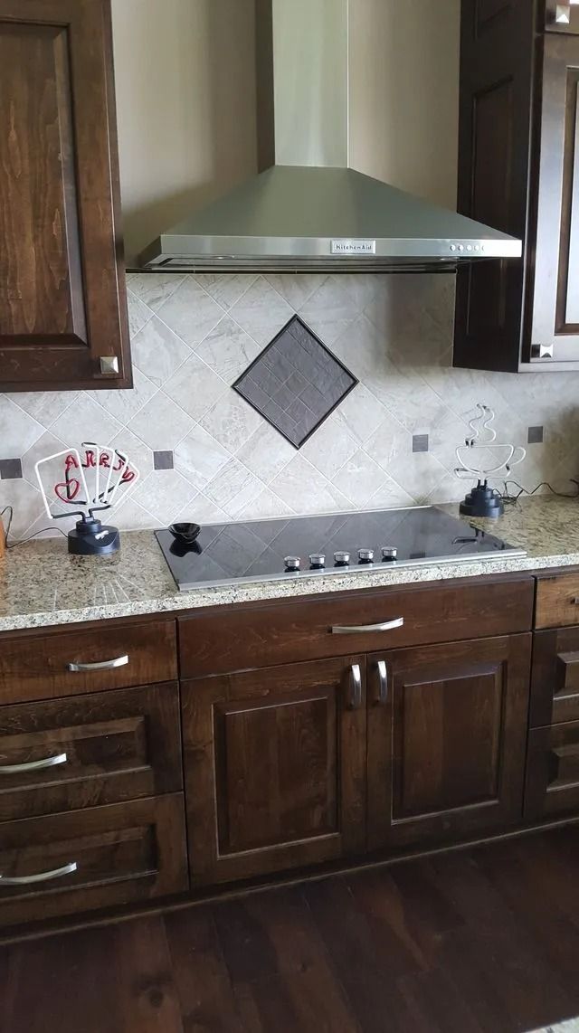 Kitchen with dark wood cabinets, granite counter, stainless range hood, and decorative tile backsplash