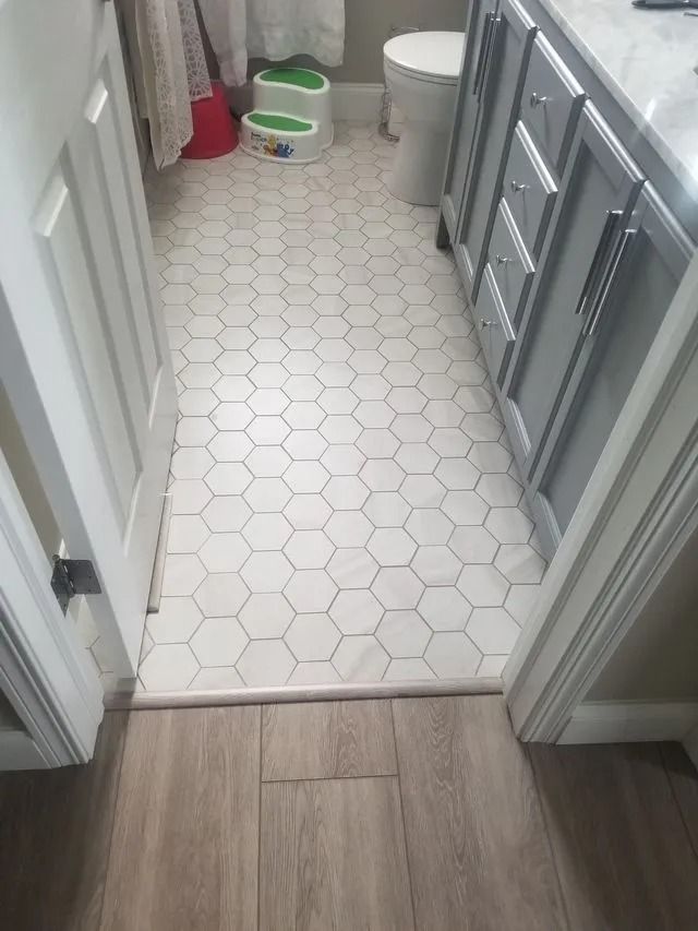 Small bathroom with white hex tile floor, gray vanity, and a green-and-white cat litter box near the back wall.