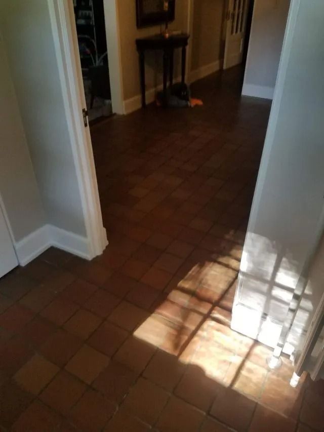 Sunlit hallway with brown tiled floor and doorway leading into a dim room
