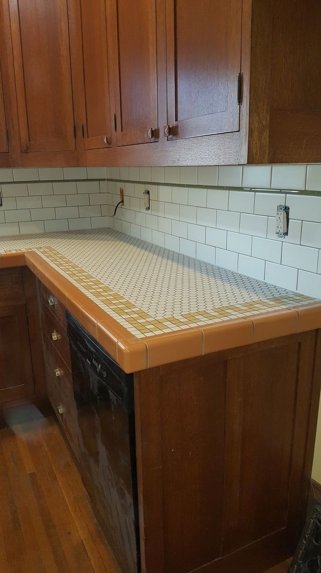 Kitchen countertop with patterned tile and wooden cabinets above and below, unfinished backsplash visible.