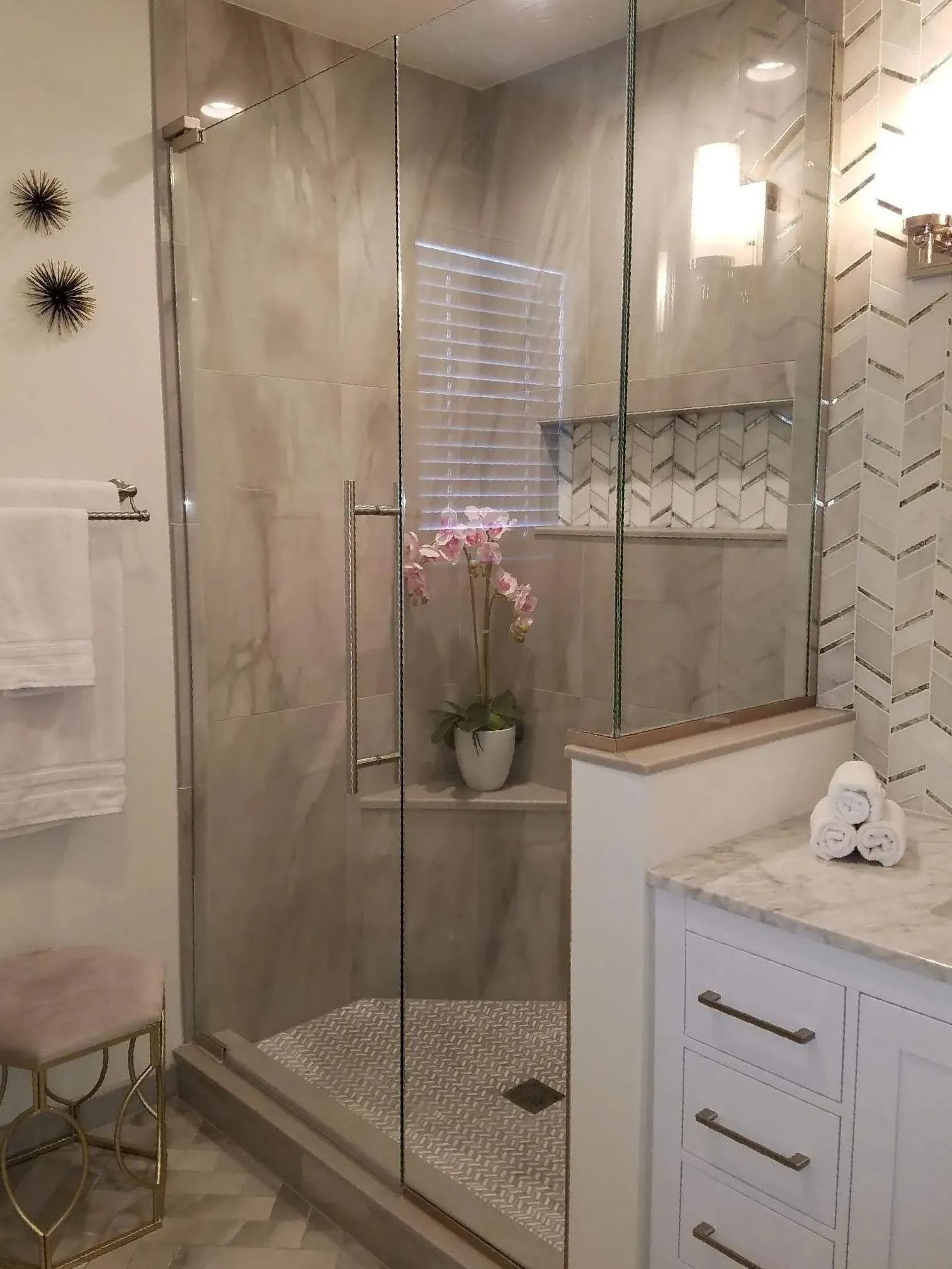 Modern beige bathroom with glass shower, marble walls, and white vanity.