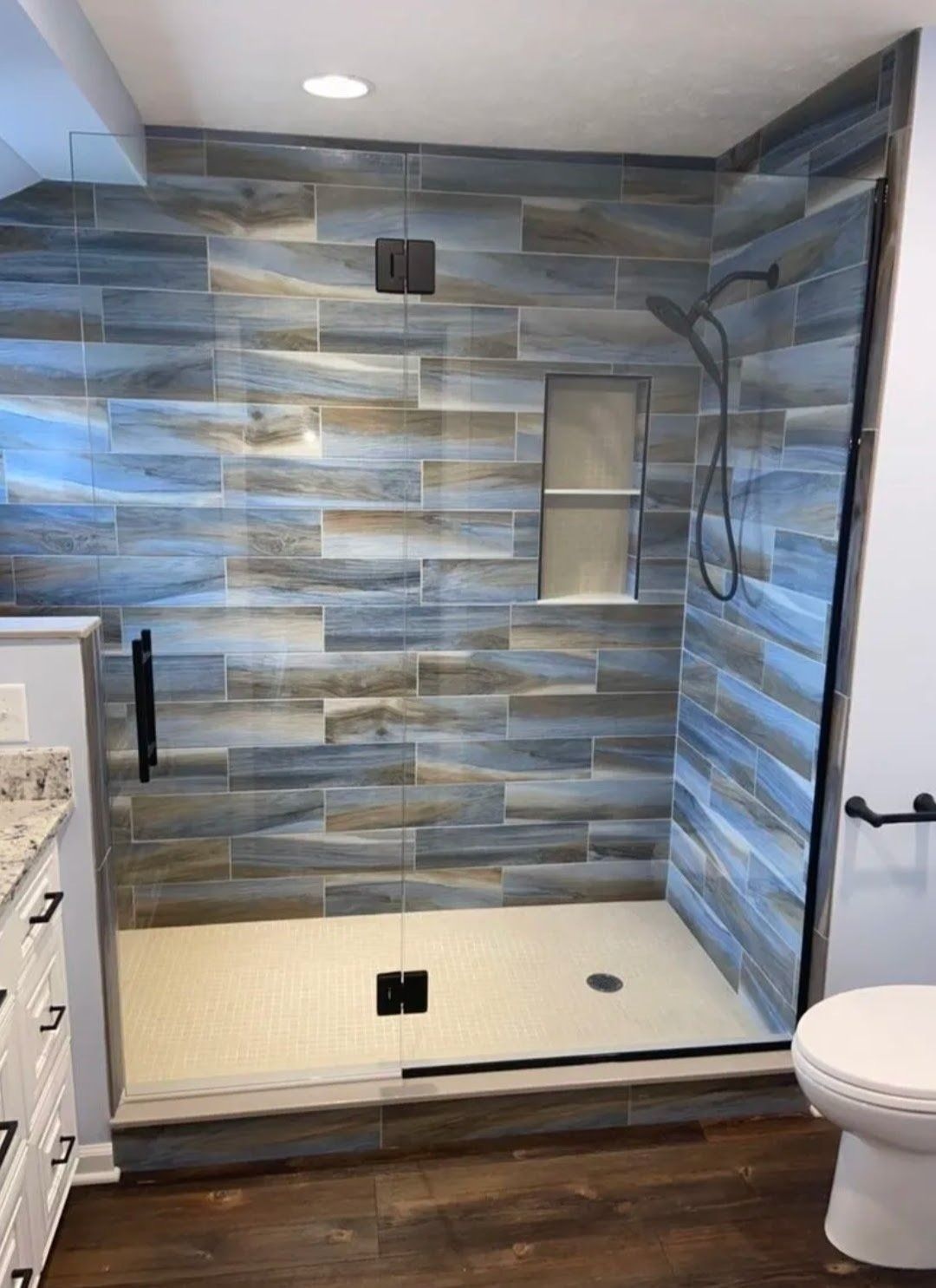 Modern bathroom shower with blue-gray tile, built-in niche, and glass door frame