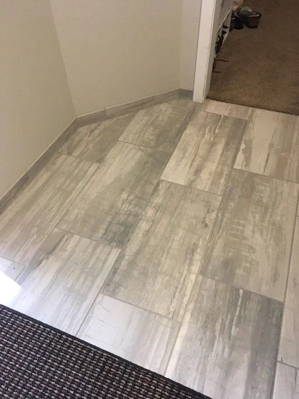 Hallway with light gray wood-look tile flooring and a dark carpet edge near a doorway.