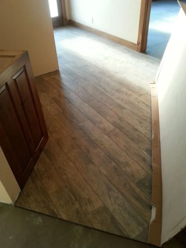 Empty hallway with wooden floorboards and open doorways, lit by daylight.