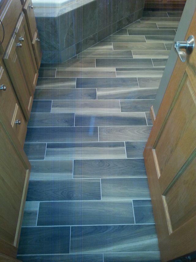 Narrow tiled bathroom floor with blue-gray rectangular tiles and wood cabinets at the sides