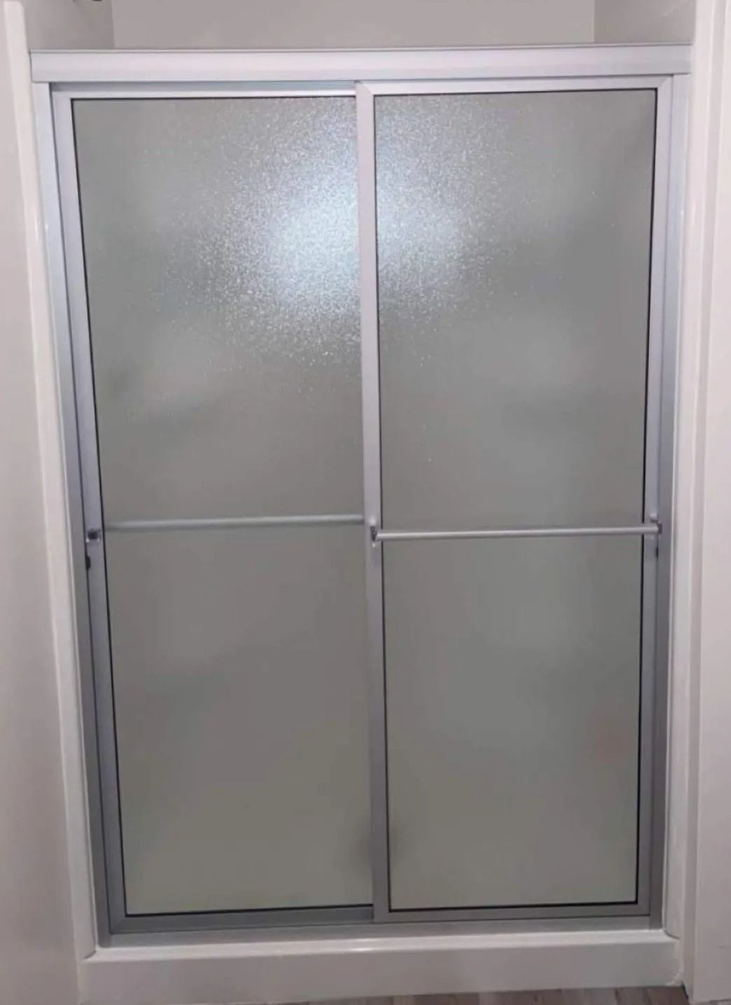 Frosted glass sliding shower door with white frame and horizontal handles