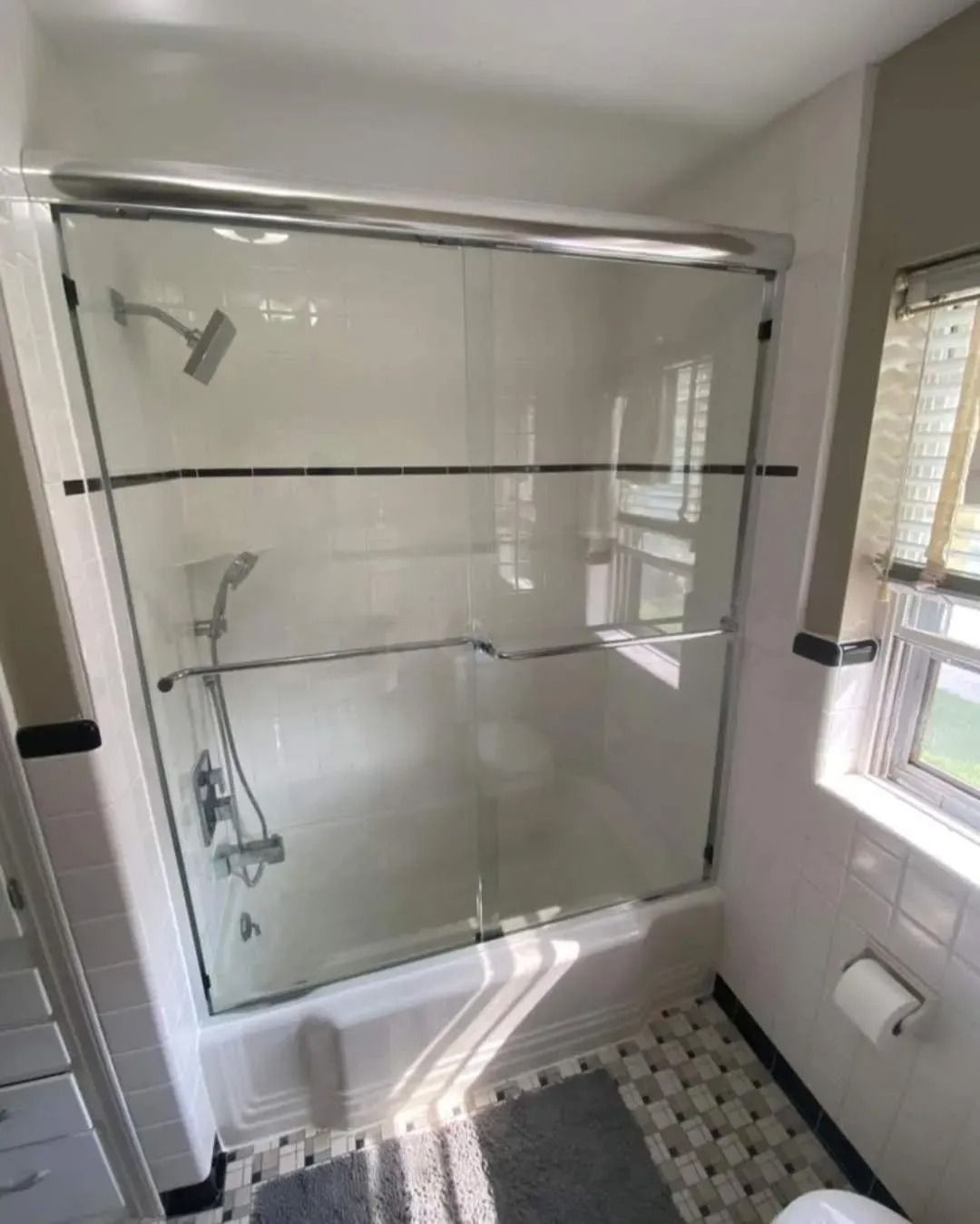 White bathroom with a glass-enclosed bathtub shower, tiled floor, and window light.