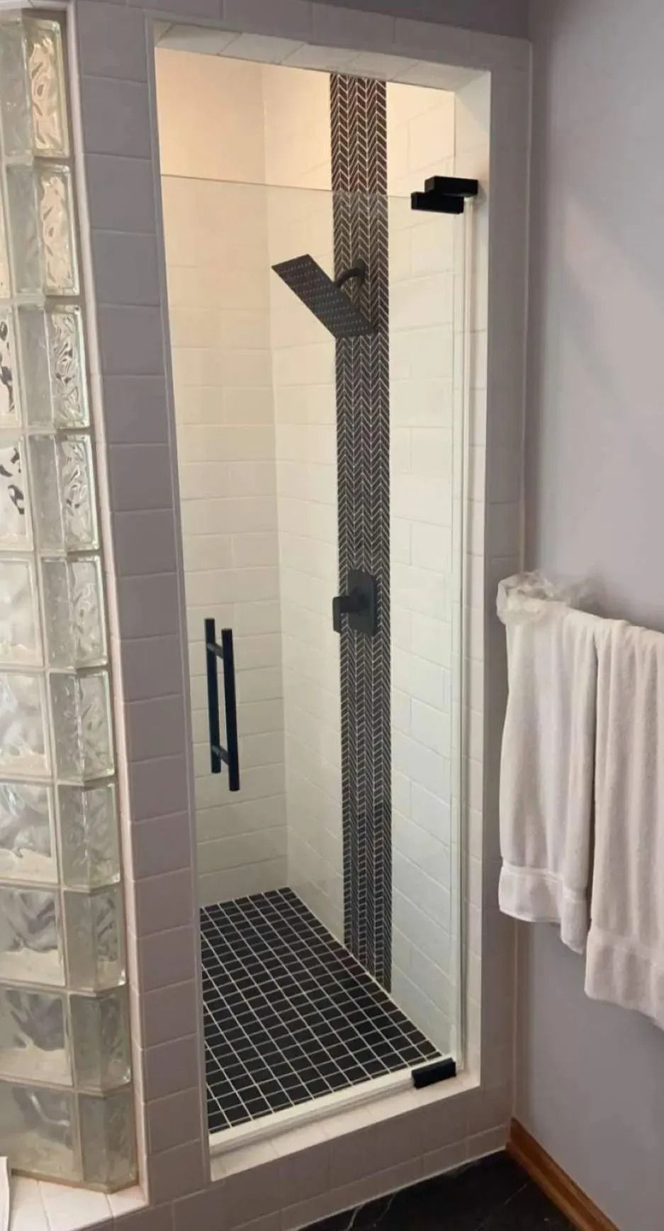 Walk-in shower with glass door, tiled floor and walls, and a towel hanging on the wall.