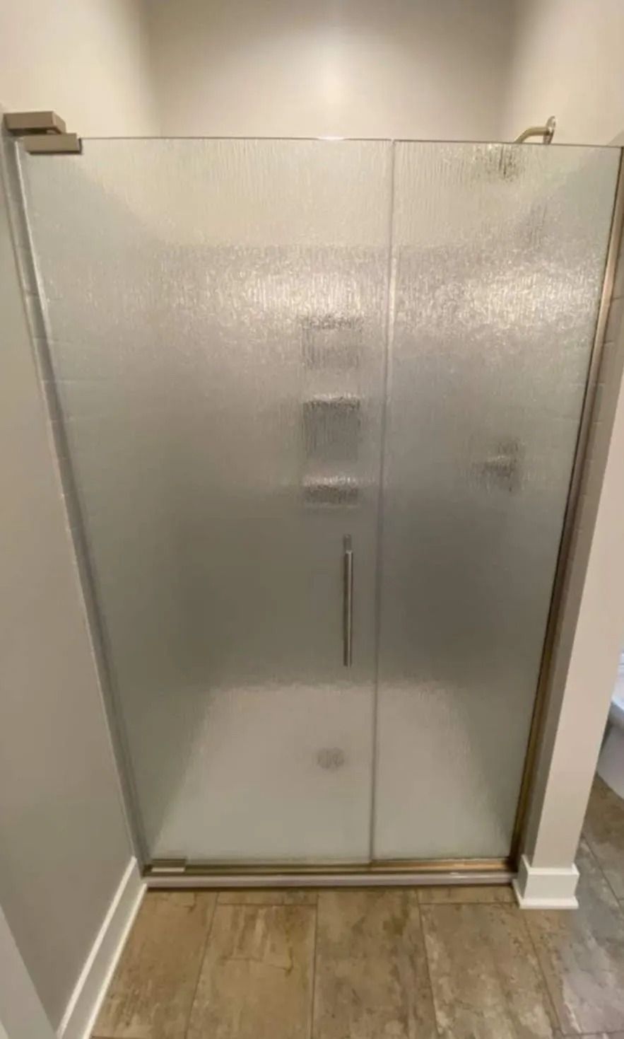 Frosted glass shower enclosure with double doors and chrome handles in a bathroom