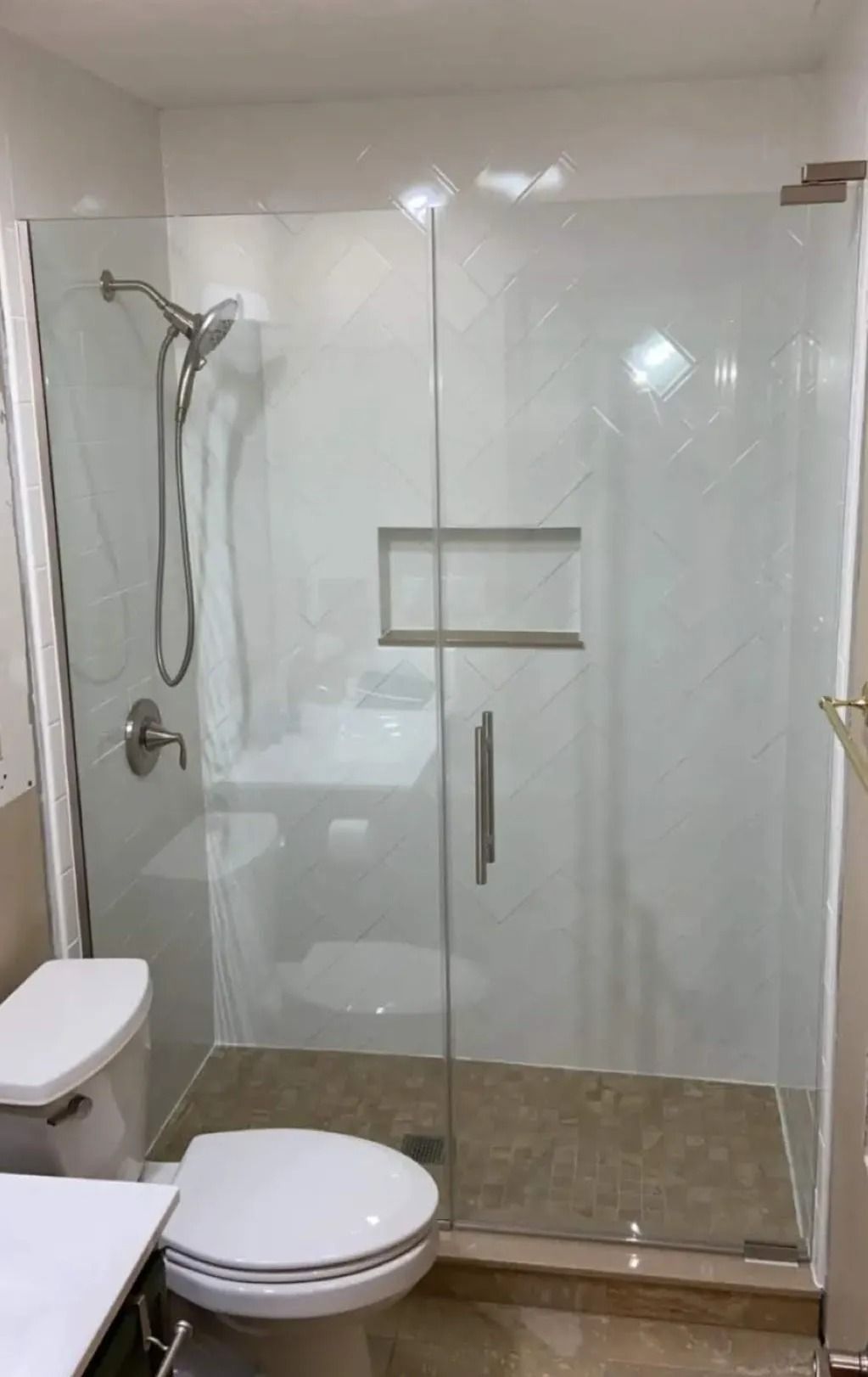 Small bathroom with glass shower, wall-mounted seat, toilet, and beige tile floor.